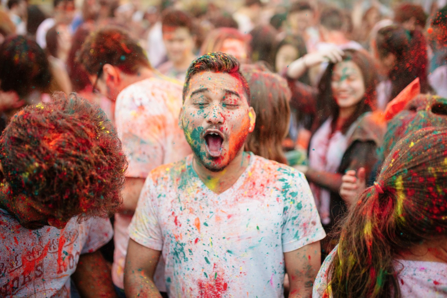 A crowd of students joyfully dance together covered in multi-coloured powder to celebrate Holi