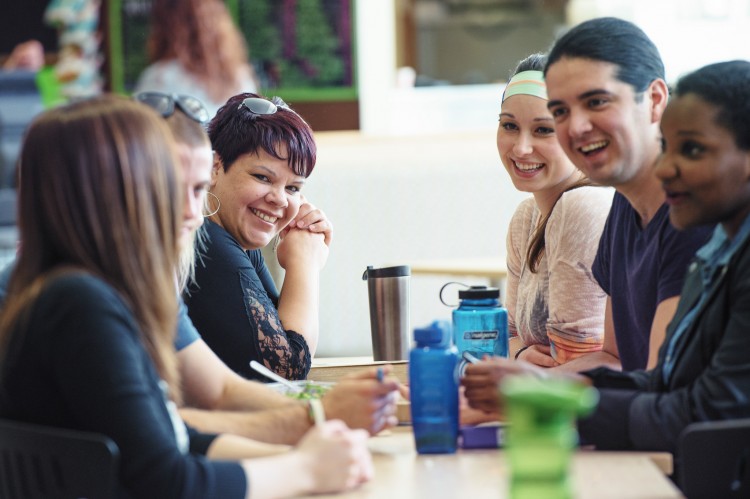 A group of students converse with one another while seated in a cafeteria