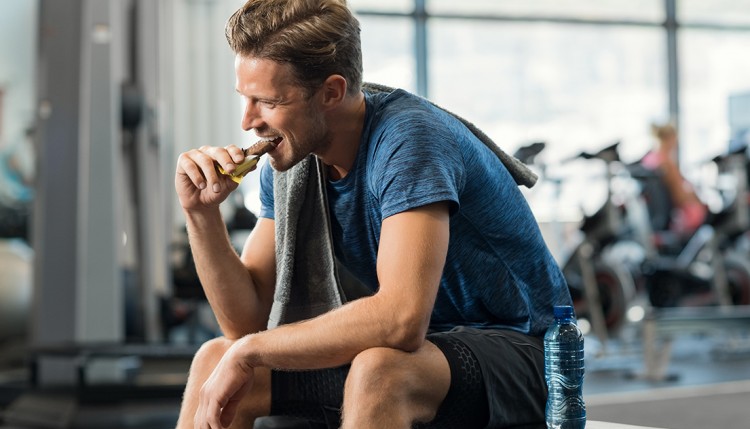 Male eating an energy bar inside a gym.